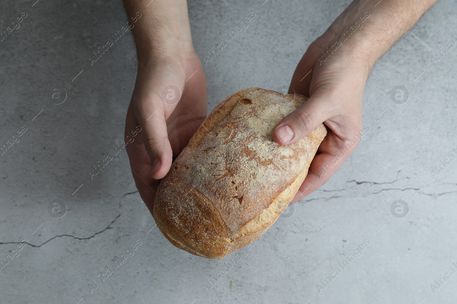 Photo of Man holding loaf of fresh bread at grey table, top view