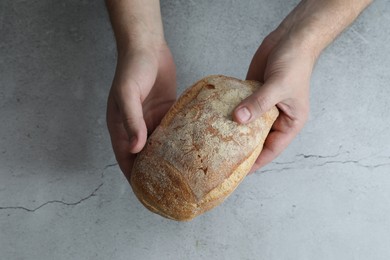 Man holding loaf of fresh bread at grey table, top view