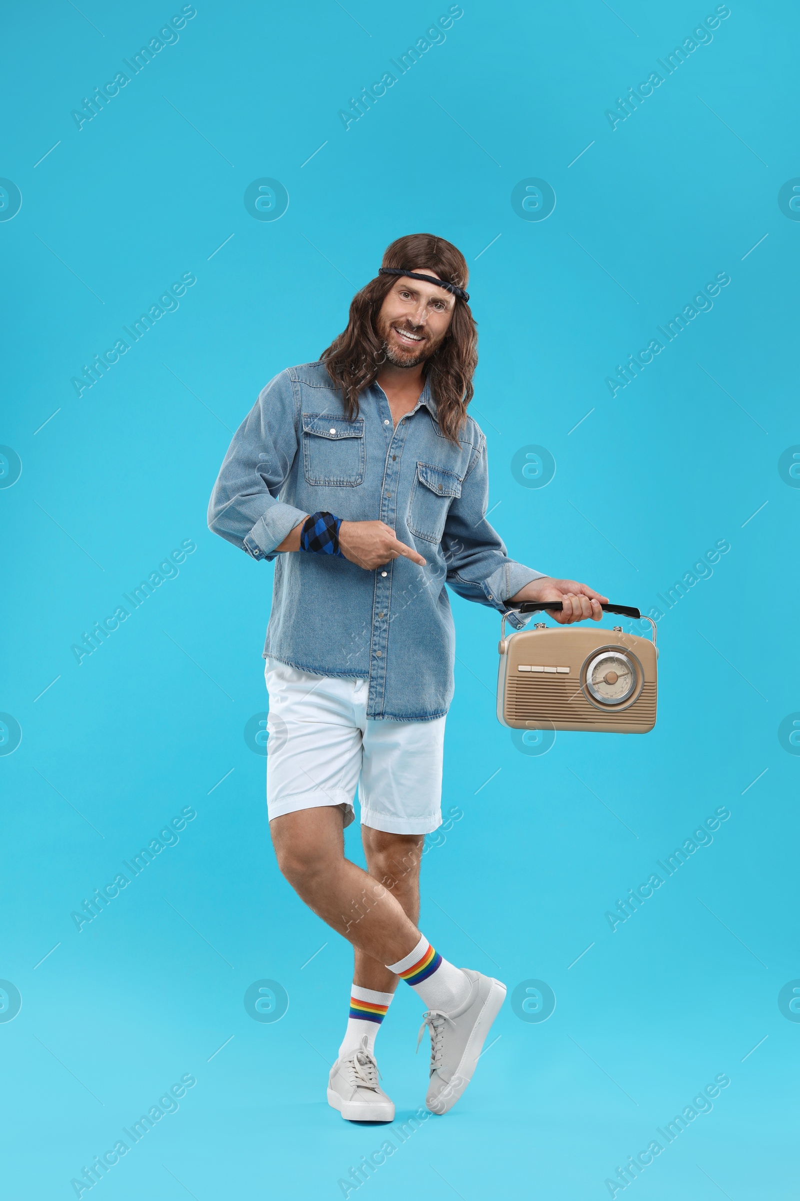 Photo of Stylish hippie man pointing at retro radio receiver on light blue background