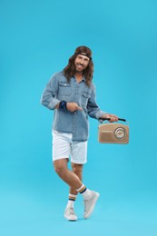 Stylish hippie man pointing at retro radio receiver on light blue background