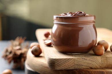 Photo of Glass jar with tasty chocolate hazelnut spread and nuts on wooden board. Space for text