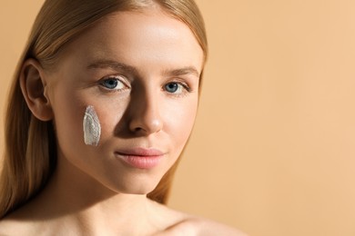 Beautiful young woman with sun protection cream on her face against beige background, closeup. Space for text