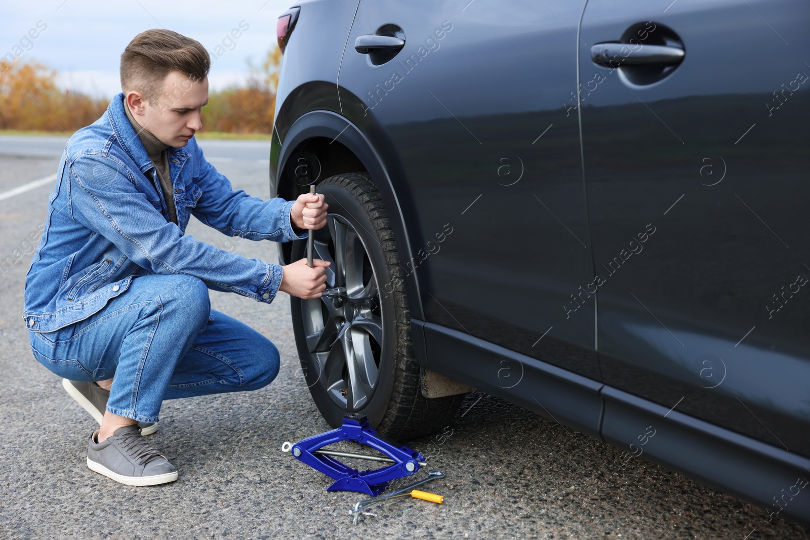 Photo of Young man changing tire of car on roadside