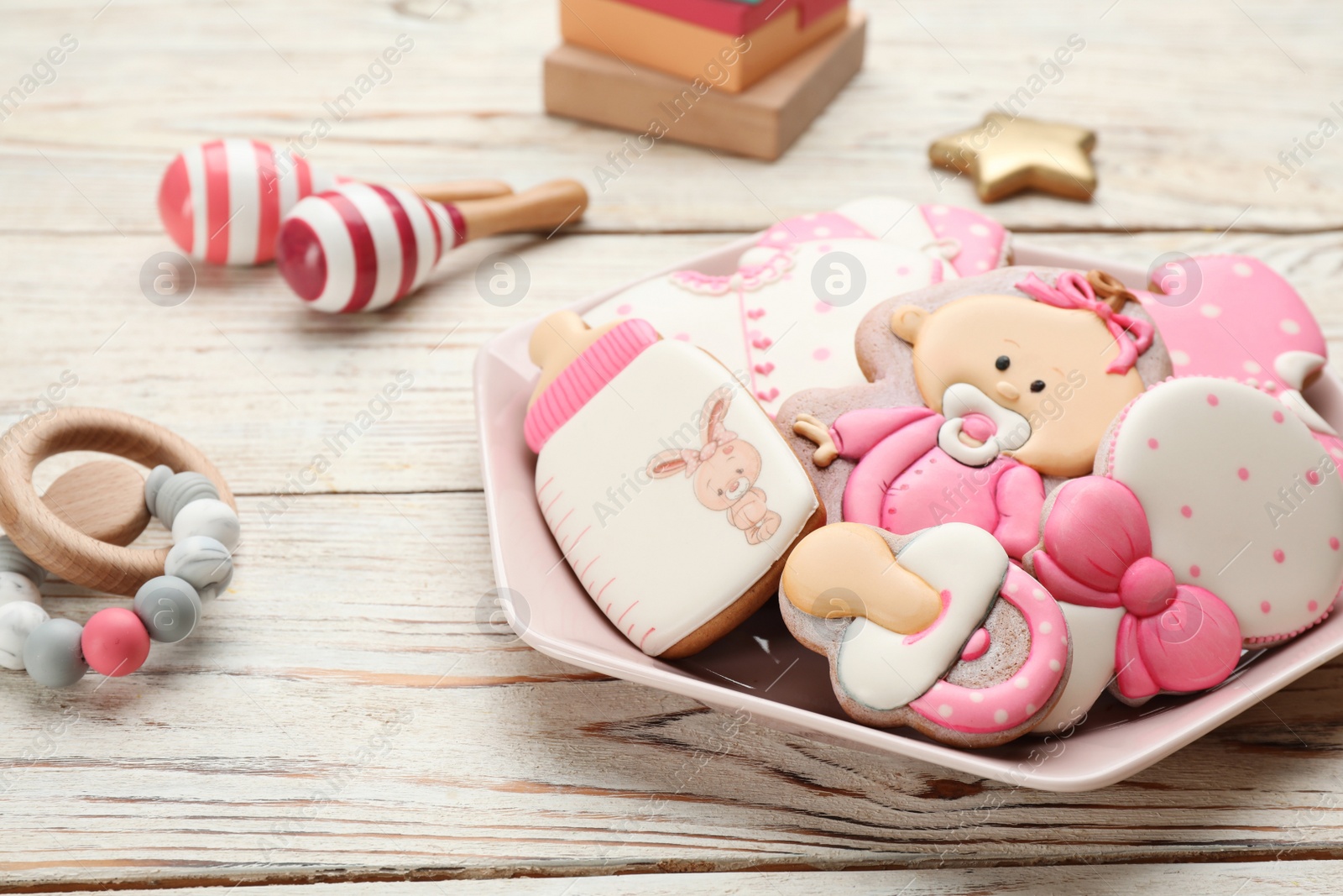 Photo of Plate of baby shower cookies and accessories on white wooden table