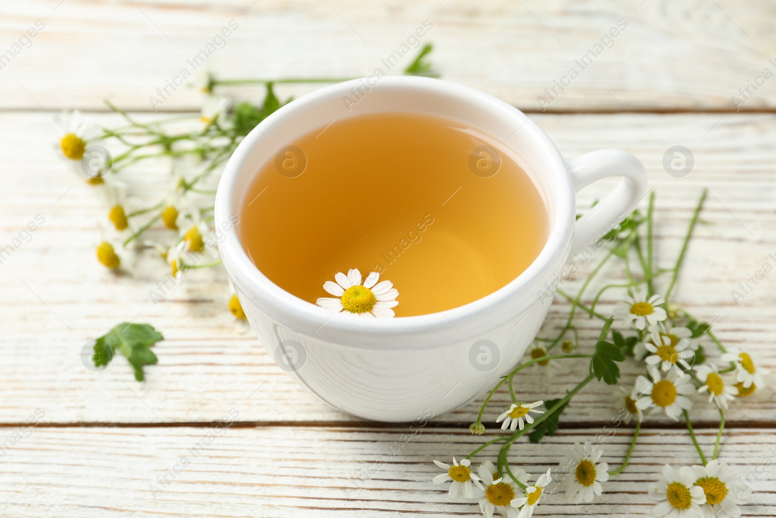 Photo of Cup of tea and chamomile flowers on white wooden table