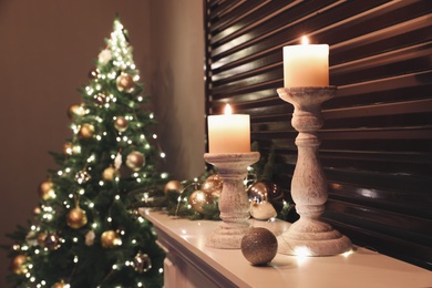 Photo of Burning candles and Christmas decor on white mantelpiece indoors