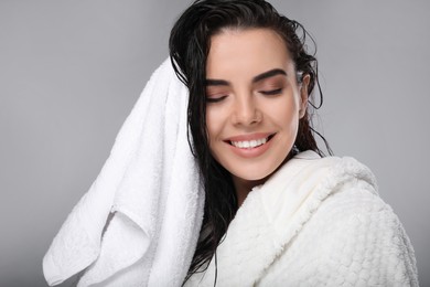 Happy young woman drying hair with towel after washing on light grey background