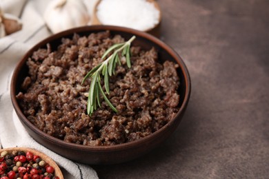 Fried ground meat in bowl and rosemary on brown textured table, closeup. Space for text