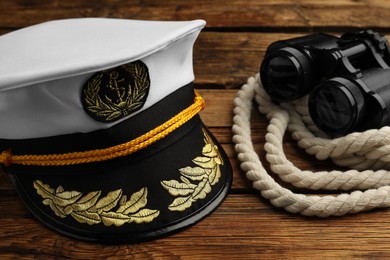 Peaked cap and rope with binoculars on wooden background, closeup