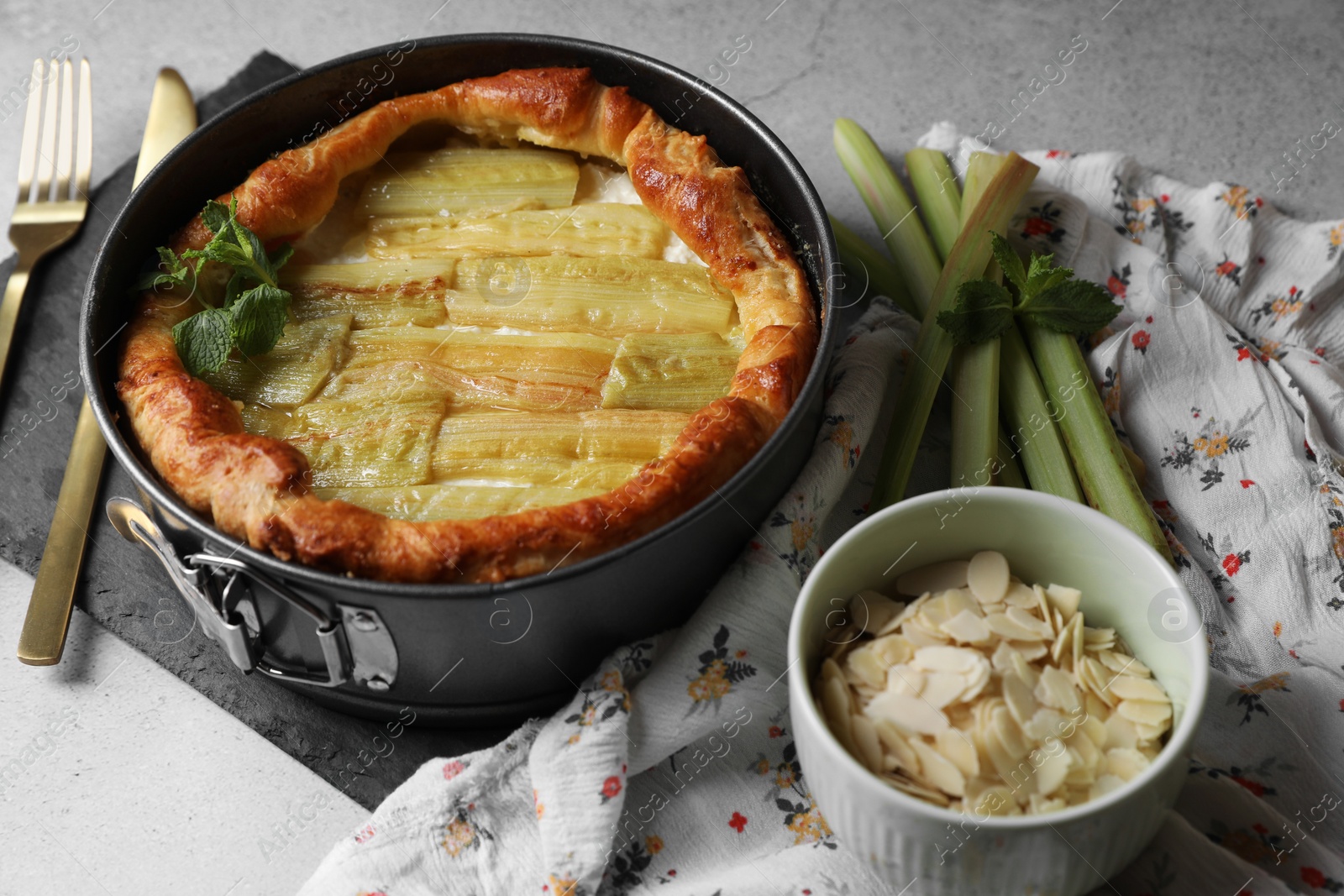 Photo of Freshly baked rhubarb pie, stalks and almond flakes on light grey table