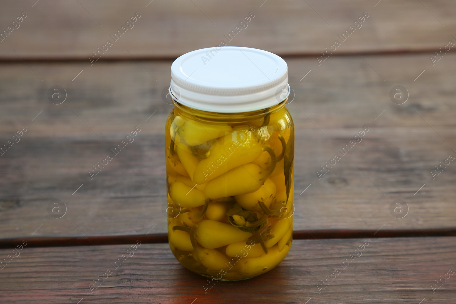 Photo of Glass jar of pickled yellow jalapeno peppers on wooden table