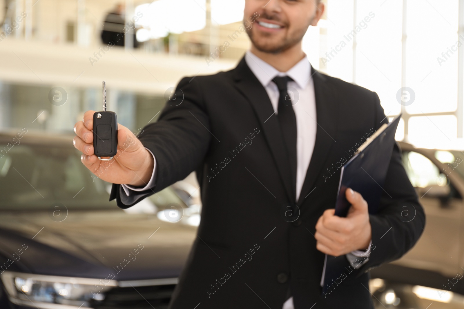 Photo of Salesman with key and clipboard in car salon, closeup