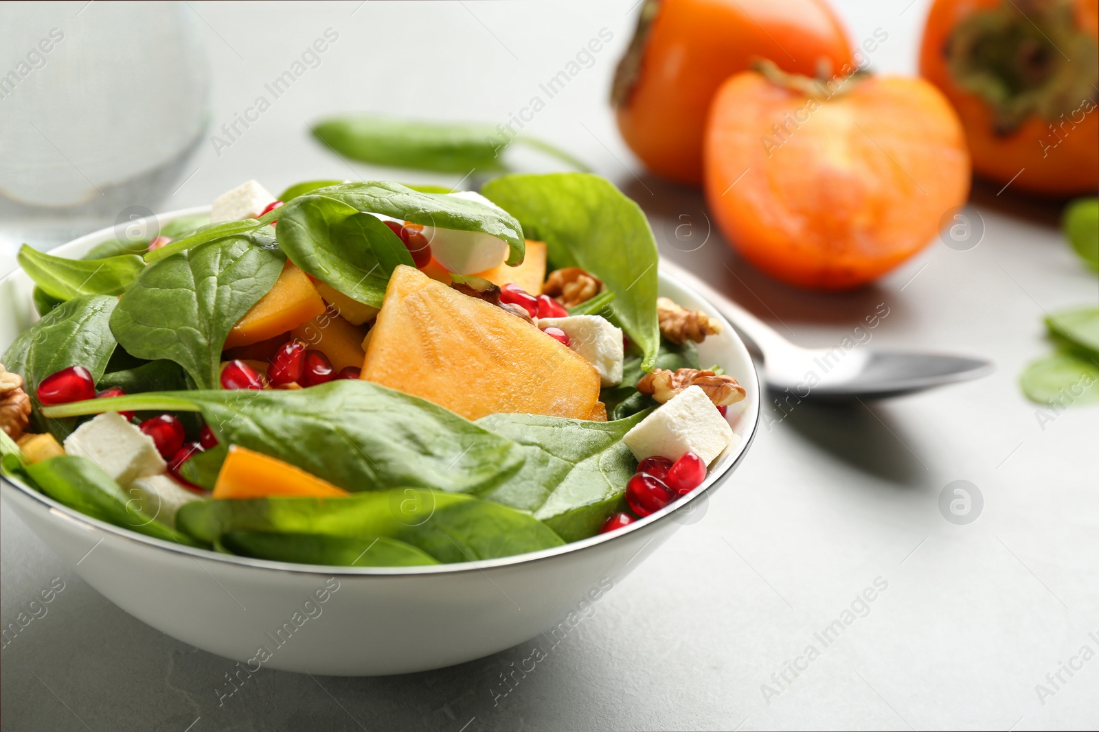 Photo of Delicious persimmon salad with pomegranate and spinach on light grey table