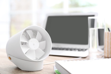 Modern portable fan on wooden table in office, space for text. Summer heat