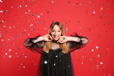 Happy young woman and confetti on red background