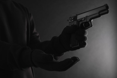 Photo of Dangerous criminal with gun on black background, closeup. Armed robbery