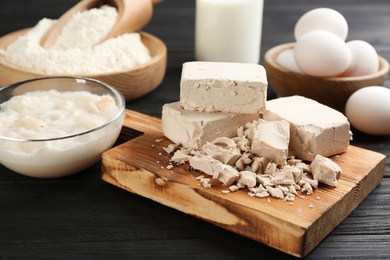 Photo of Pieces of compressed yeast near ingredients for dough on black wooden table