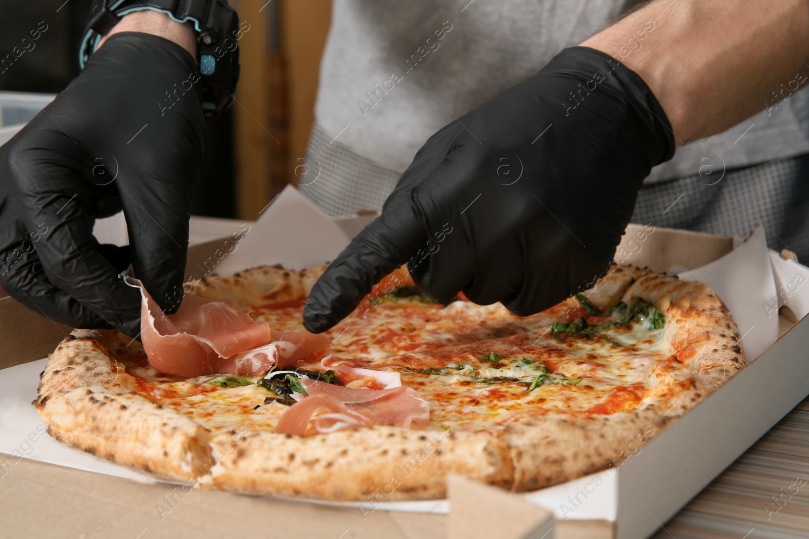 Photo of Professional chef adding prosciutto to Italian oven baked pizza in restaurant, closeup