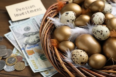 Photo of Money, card with phrase Pension Investments near many golden and quail eggs in nest on wooden table