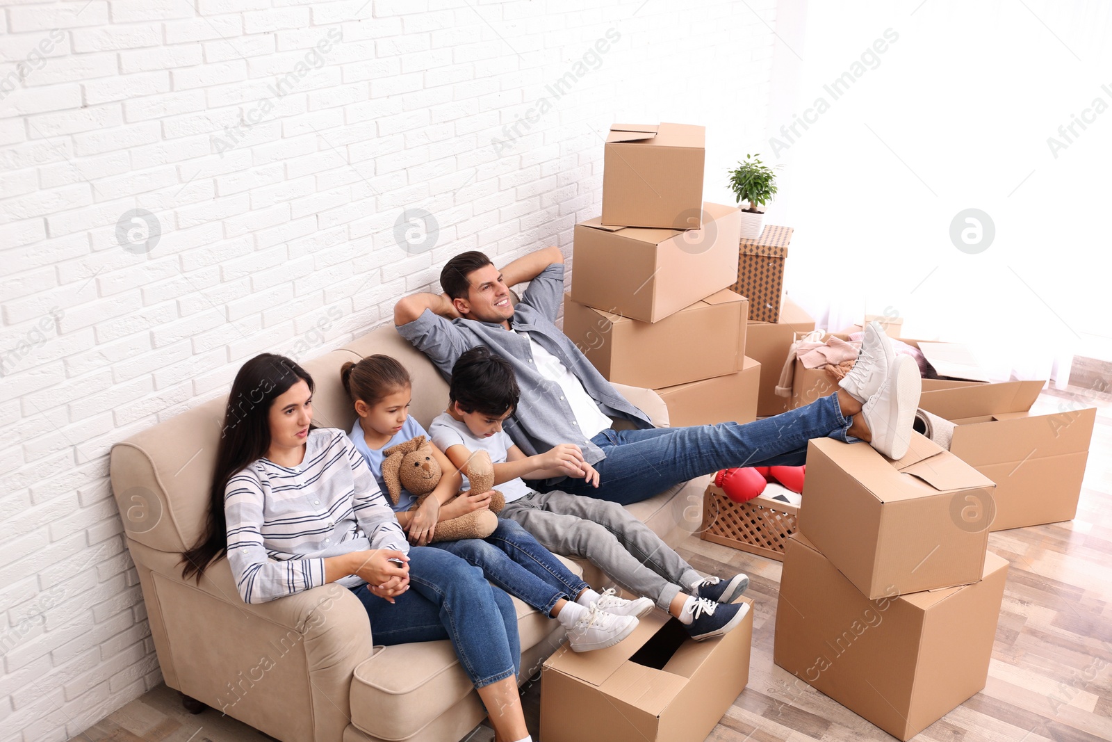 Photo of Happy family resting in room with cardboard boxes on moving day