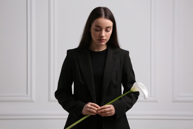 Sad woman with calla lily flower near white wall. Funeral ceremony