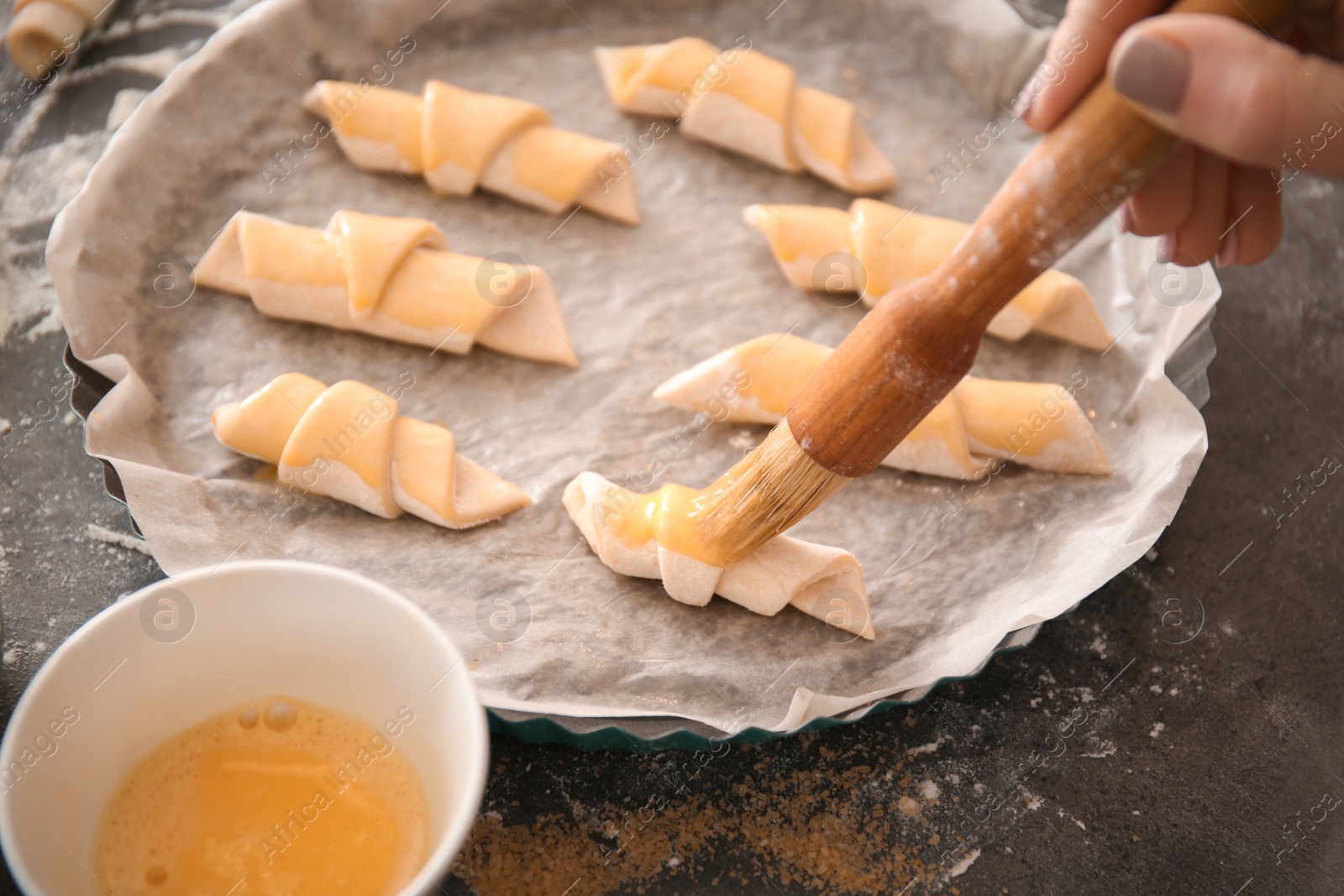 Photo of Woman spreading egg yolk on croissants, closeup