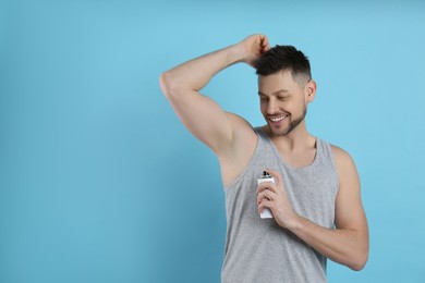 Photo of Handsome man applying deodorant on turquoise background. Space for text