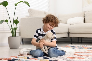 Photo of Little boy with cute puppy on carpet at home