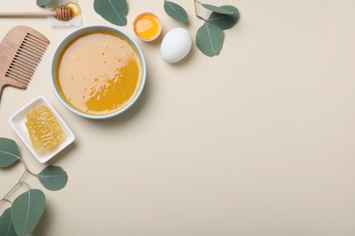 Homemade hair mask in bowl, ingredients and bamboo comb on beige background, flat lay. Space for text