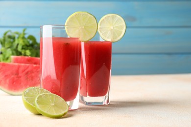 Photo of Tasty summer watermelon drink with lime in glasses on table against light blue background. Space for text