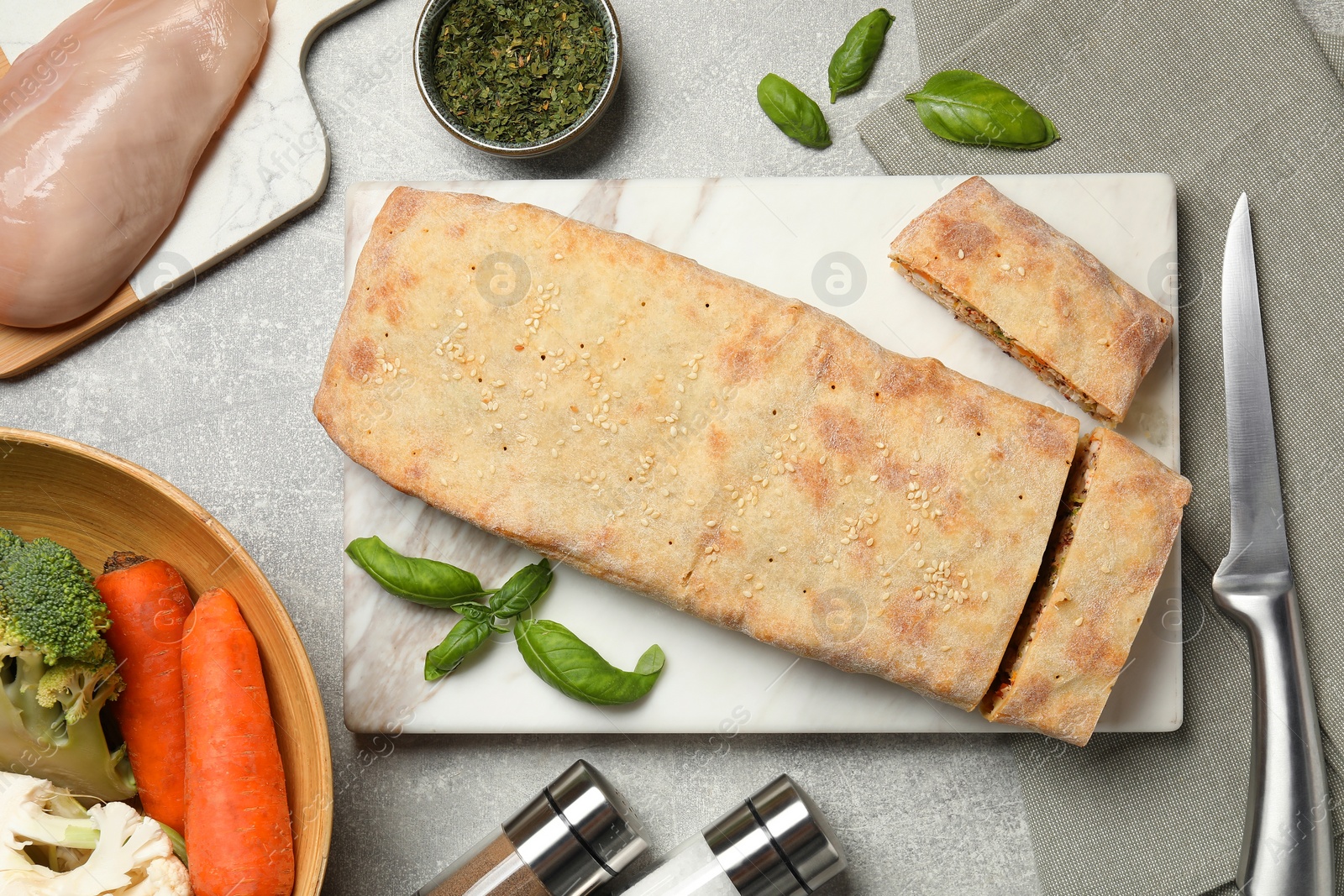 Photo of Delicious strudel with chicken, vegetables and basil served on grey table, flat lay