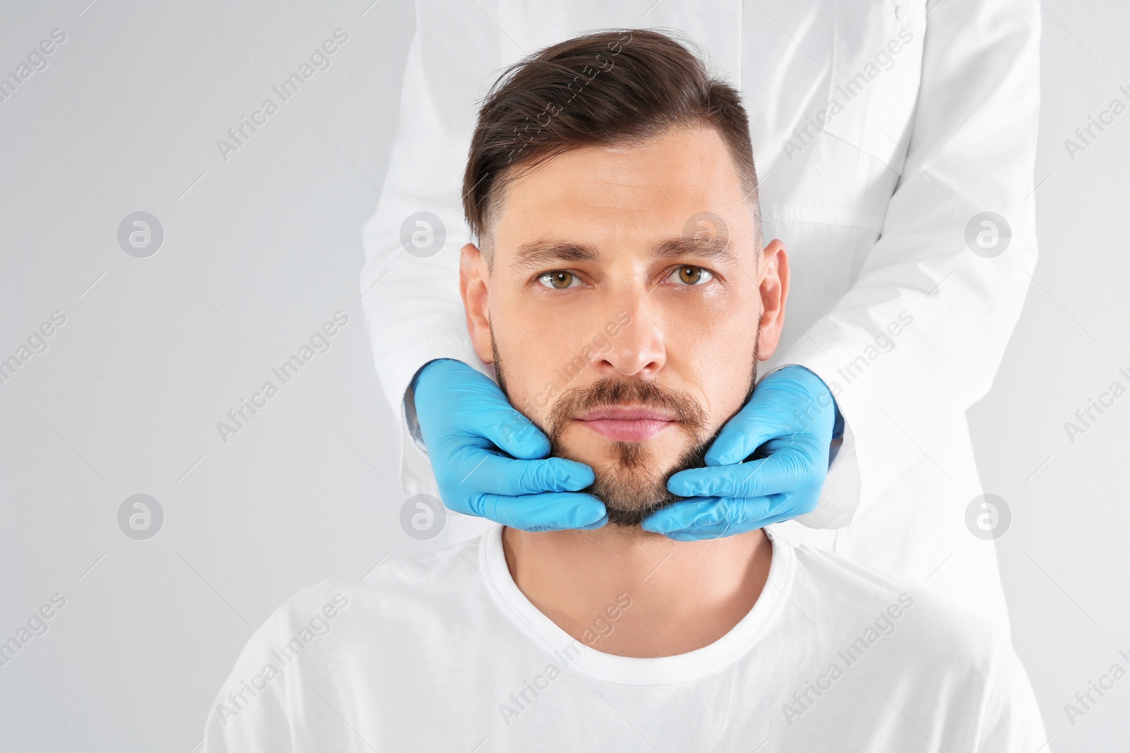 Photo of Doctor examining mature man face before cosmetic surgery on white background