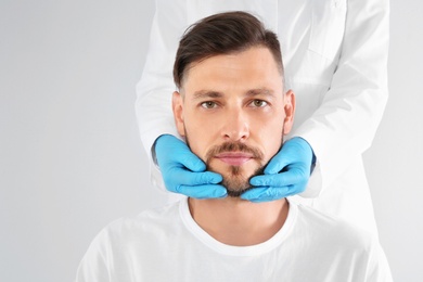 Doctor examining mature man face before cosmetic surgery on white background