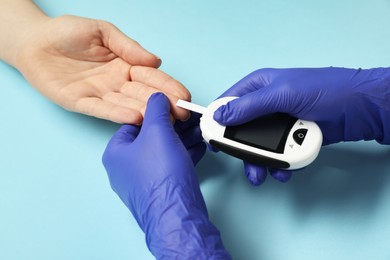 Diabetes. Doctor checking patient's blood sugar level with glucometer on light blue background, closeup