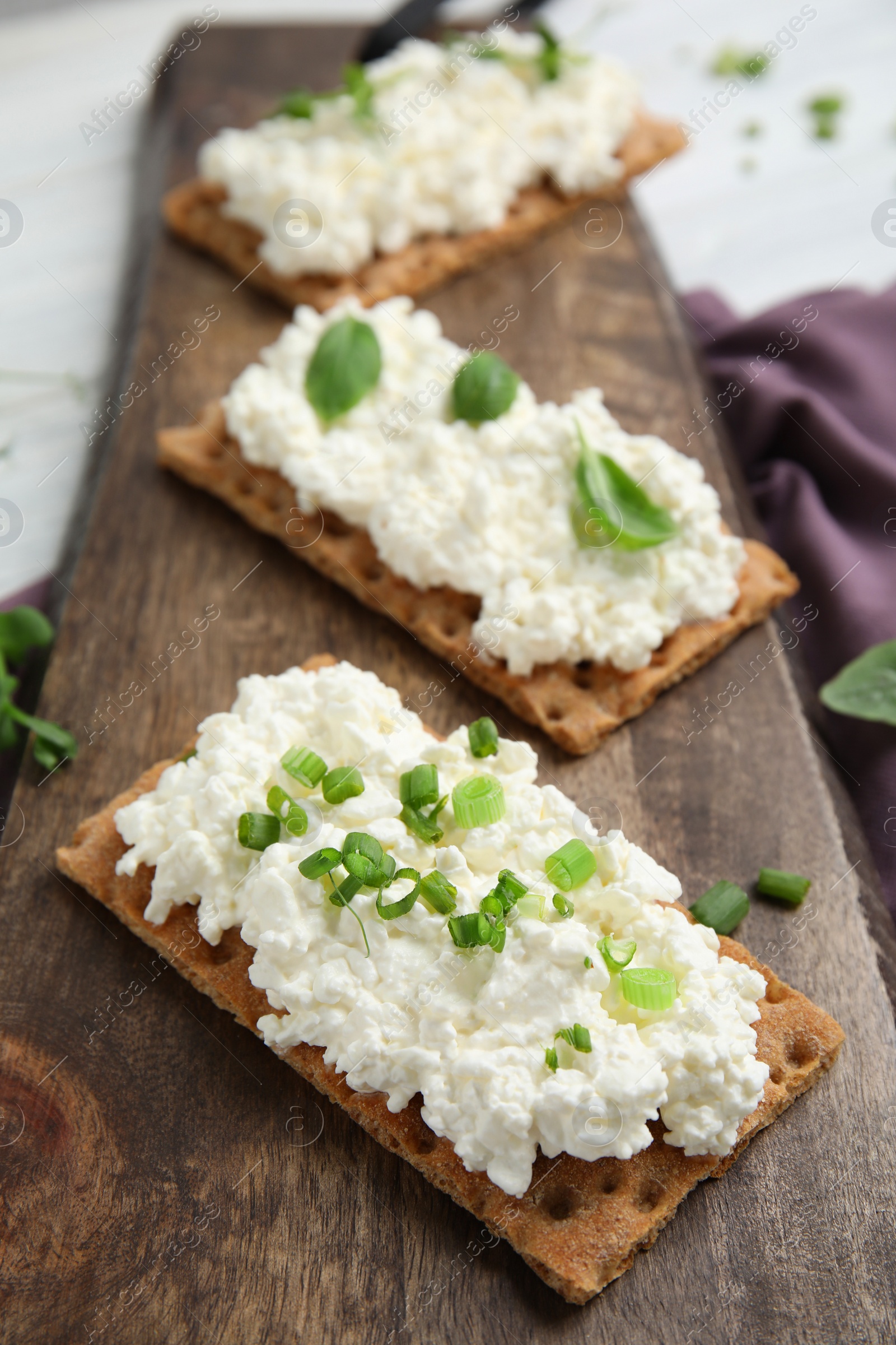 Photo of Crispy crackers with cottage cheese and different herbs on wooden board, closeup