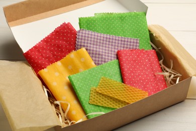 Colorful beeswax food wraps in box on white wooden table, closeup