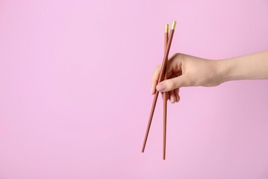 Photo of Woman holding pair of wooden chopsticks on pink background, closeup. Space for text