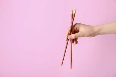 Woman holding pair of wooden chopsticks on pink background, closeup. Space for text