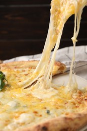 Photo of Taking piece of delicious cheese pizza at table, closeup