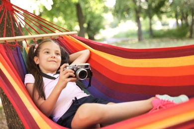 Photo of Little girl with camera in hammock outdoors. Summer camp