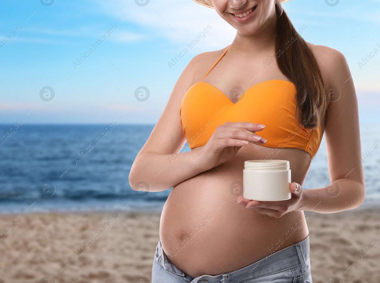 Image of Young pregnant woman with sun protection cream on beach, closeup