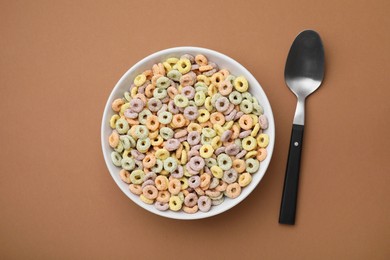 Photo of Tasty cereal rings in bowl and spoon on brown table, flat lay