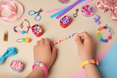 Photo of Child making beaded jewelry and different supplies on beige background, above view. Handmade accessories