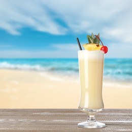 Image of Tasty Pina Colada cocktail on wooden table near ocean. Space for text