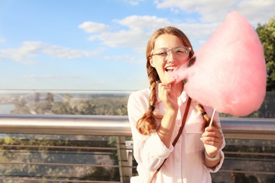 Photo of Young woman with cotton candy outdoors on sunny day. Space for text