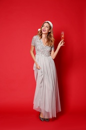 Photo of Happy woman in Santa hat with glass of champagne on red background. Christmas party