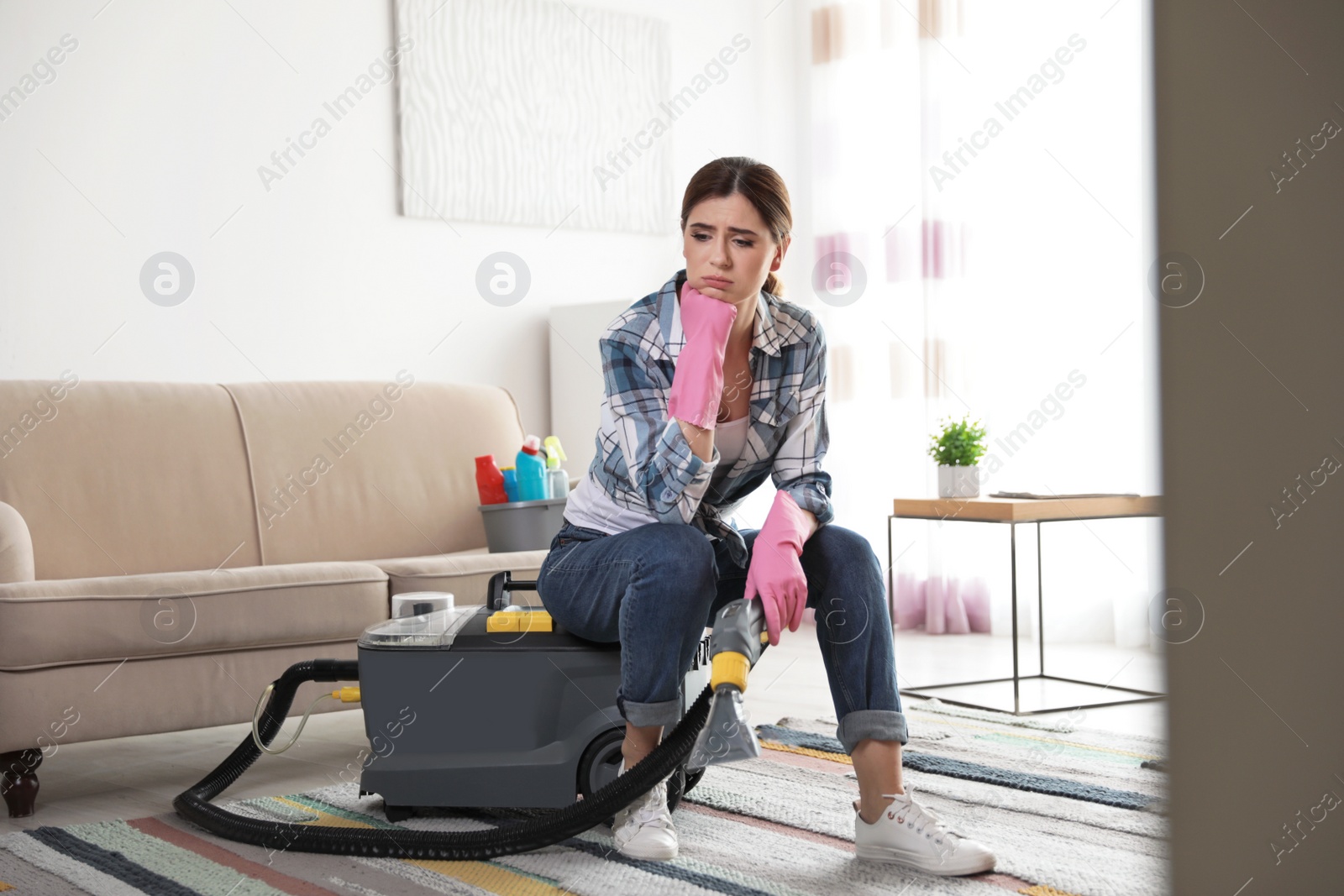 Photo of Tired woman sitting on vacuum cleaner at home