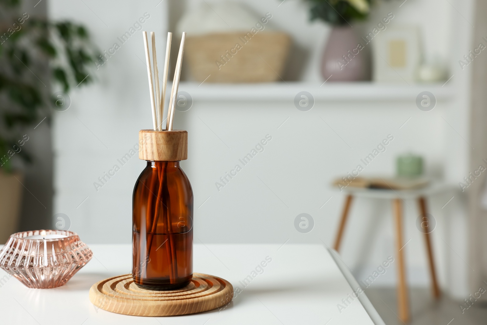 Photo of Aromatic reed air freshener and candle on white table in room. Space for text