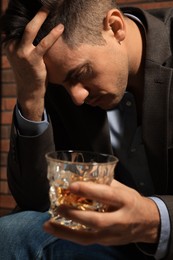Photo of Addicted man with glass of alcoholic drink near red brick wall, closeup