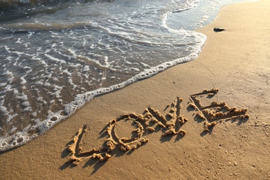 Photo of Word LOVE written on sandy beach near sea. Wedding concept